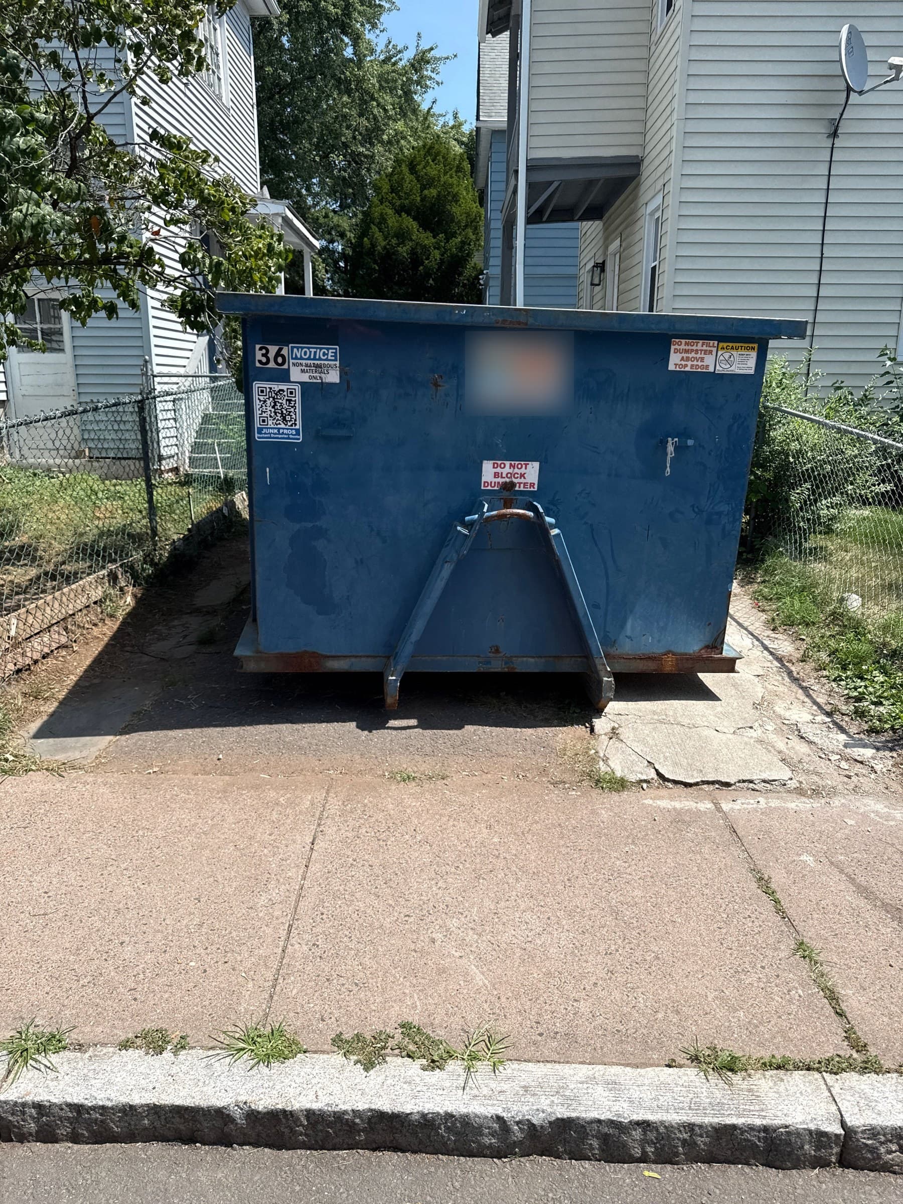 Blue roll-off dumpster in a narrow driveway between houses