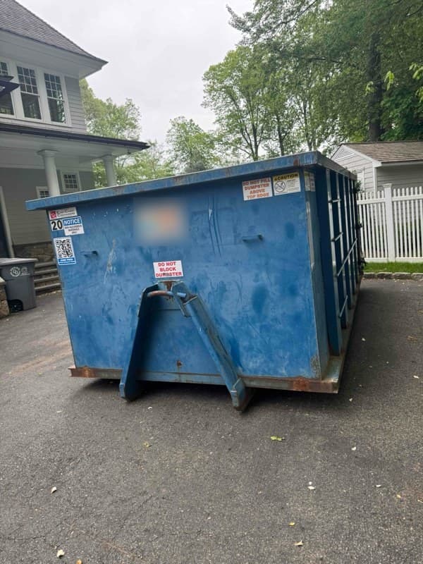 Blue roll-off dumpster on a driveway by a grey house