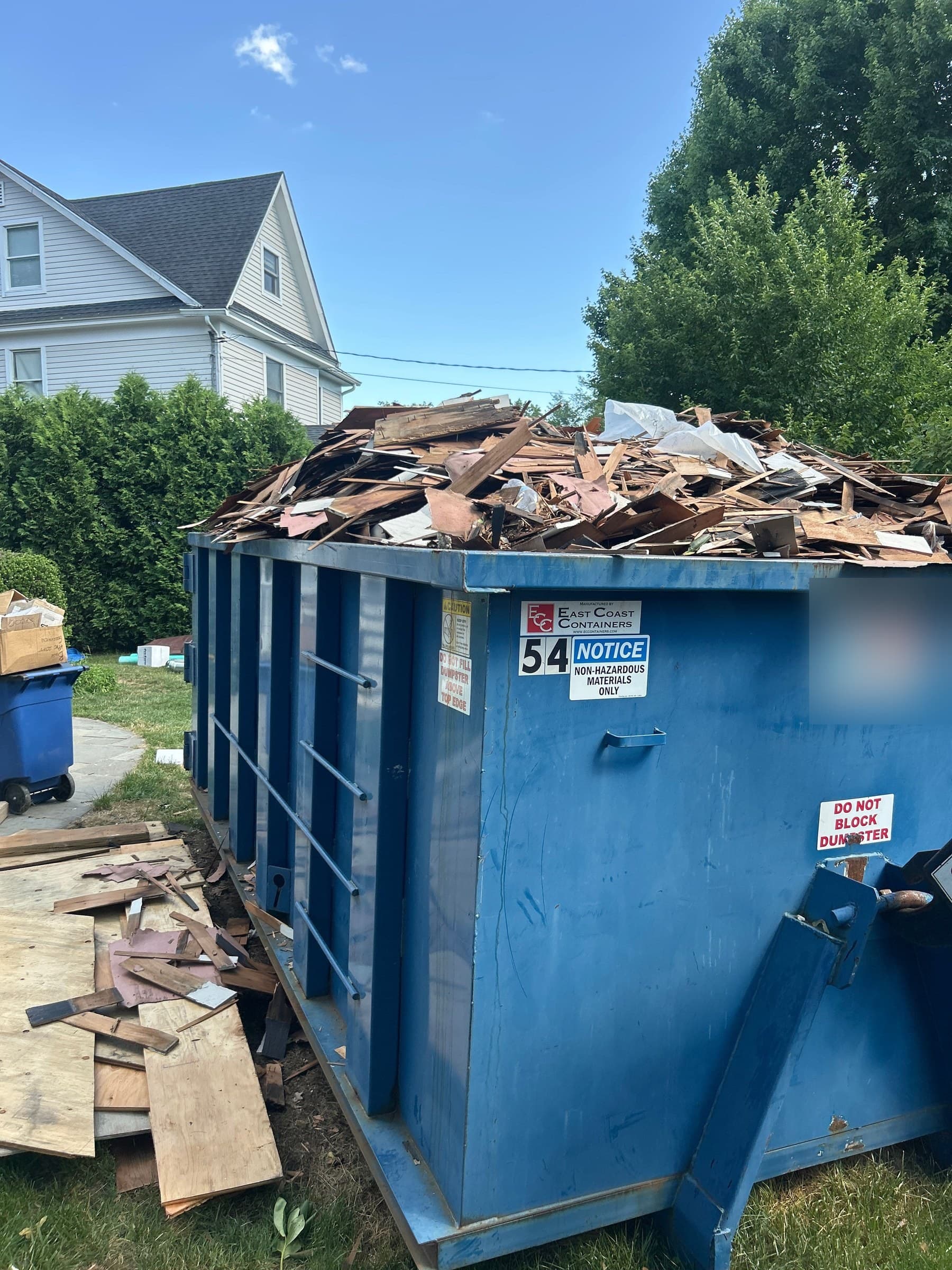 Roll-off dumpster heaped with roofing and wood debris on a lawn
