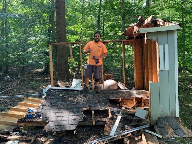 Grizzly Junk Pros crew member demolishing a residential deck in a wooded yard, debris staged for hauling