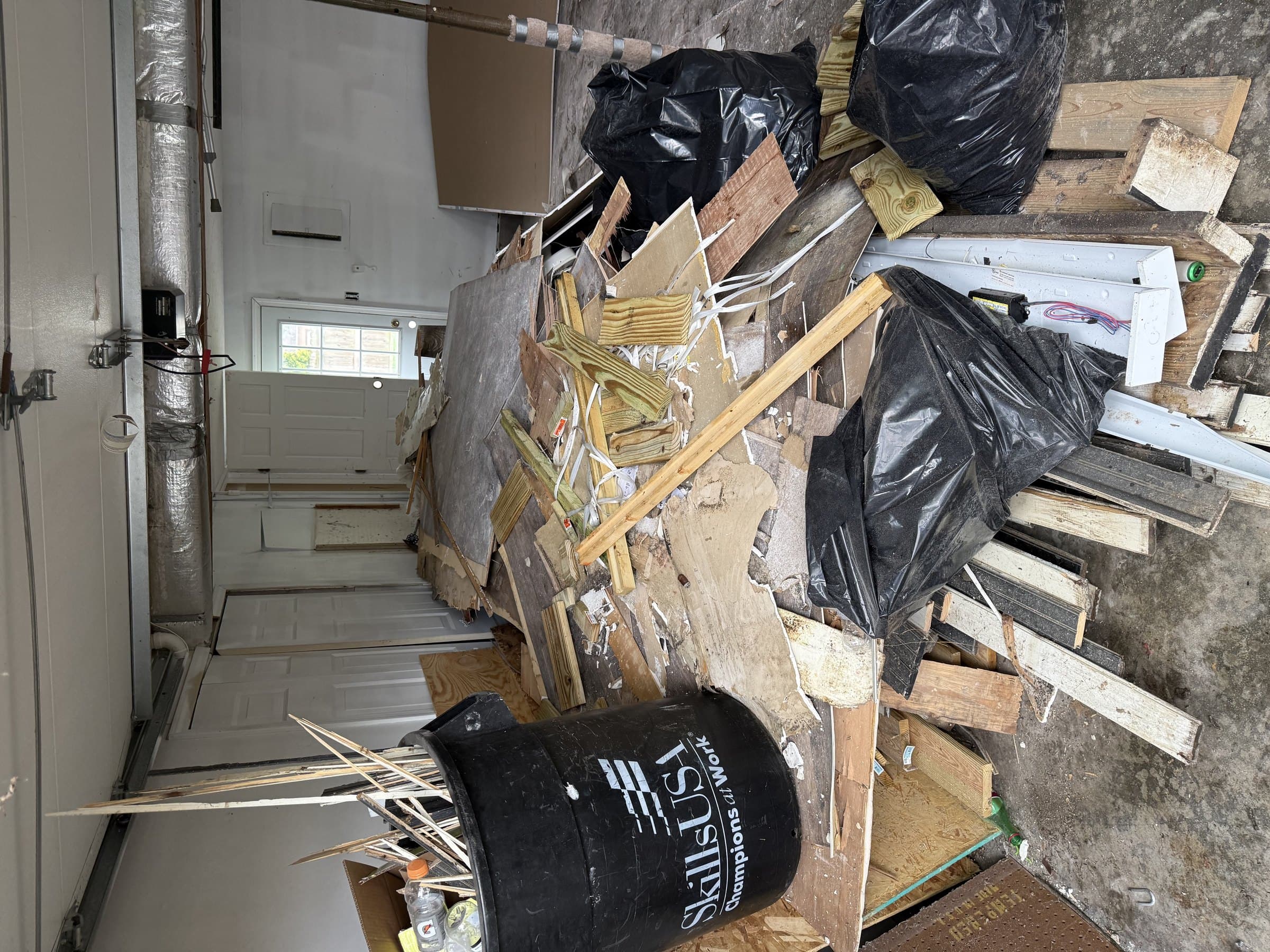 garage interior with junk removal debris pile including black trash bags wooden boards cardboard and a black utility by Grizzly Junk Pros