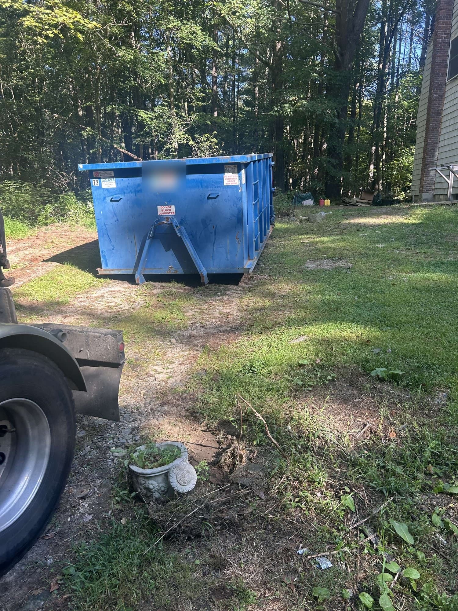 Blue roll-off dumpster on a lawn path by the woods