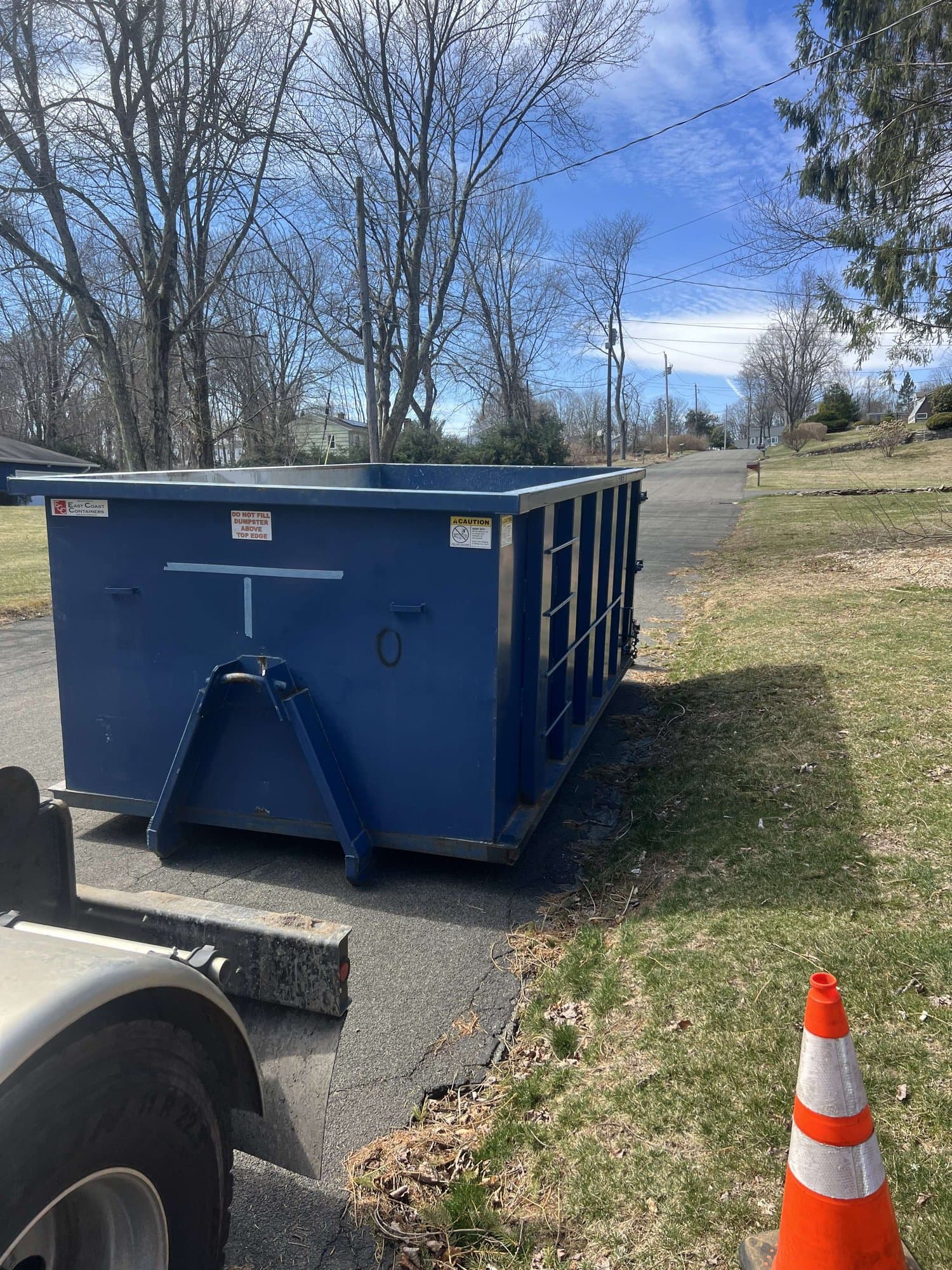 Blue roll-off dumpster set at the roadside with a safety cone