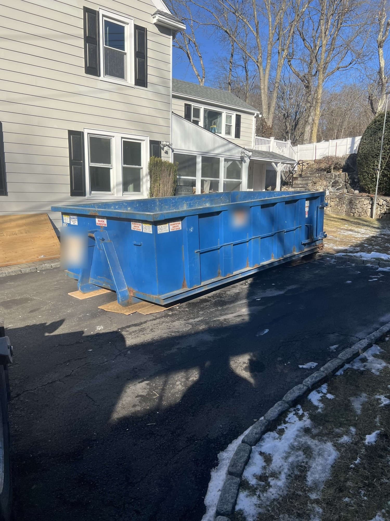 Blue roll-off dumpster on plywood boards in a driveway