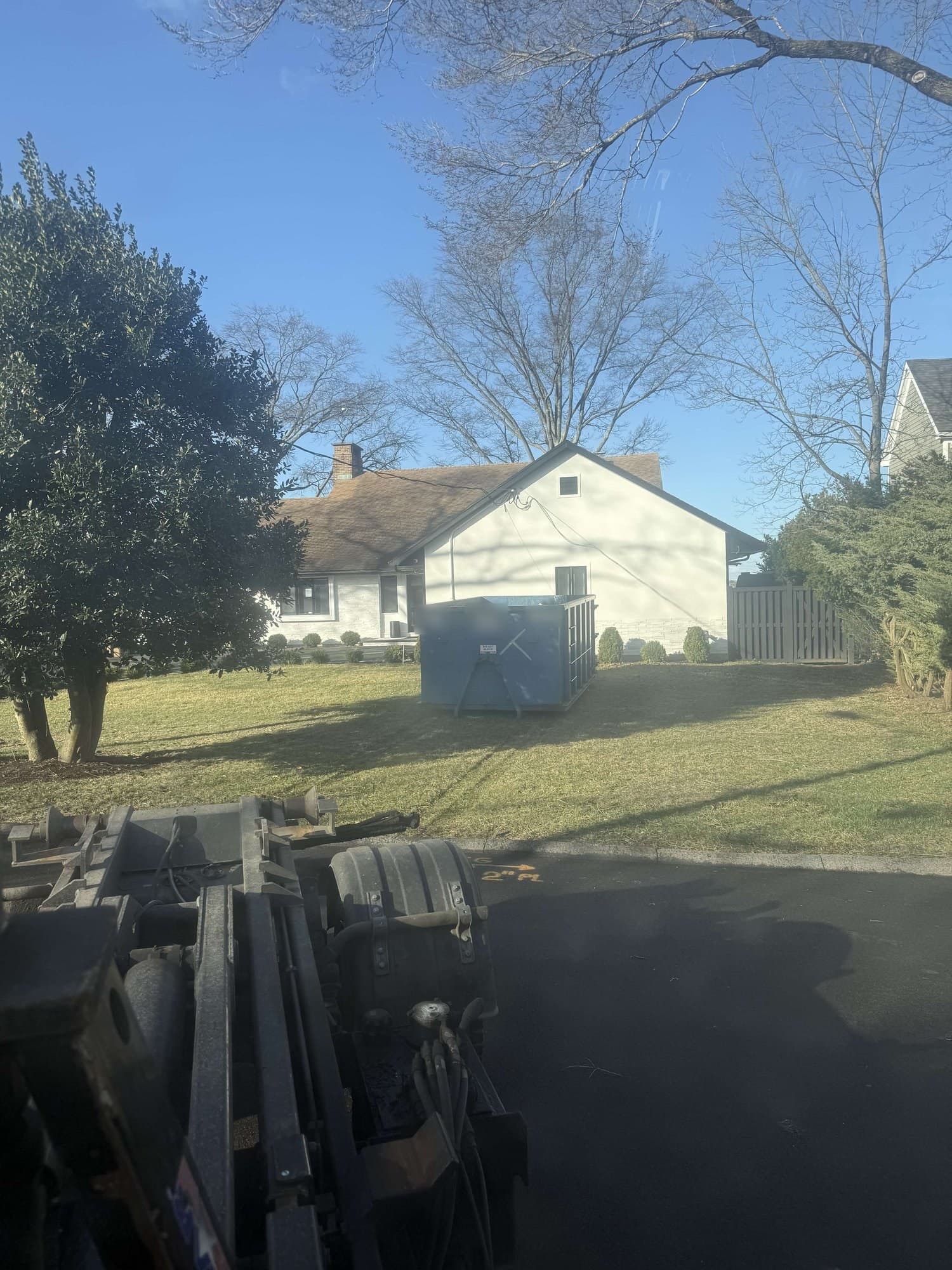 Blue roll-off dumpster on a lawn in front of a white house