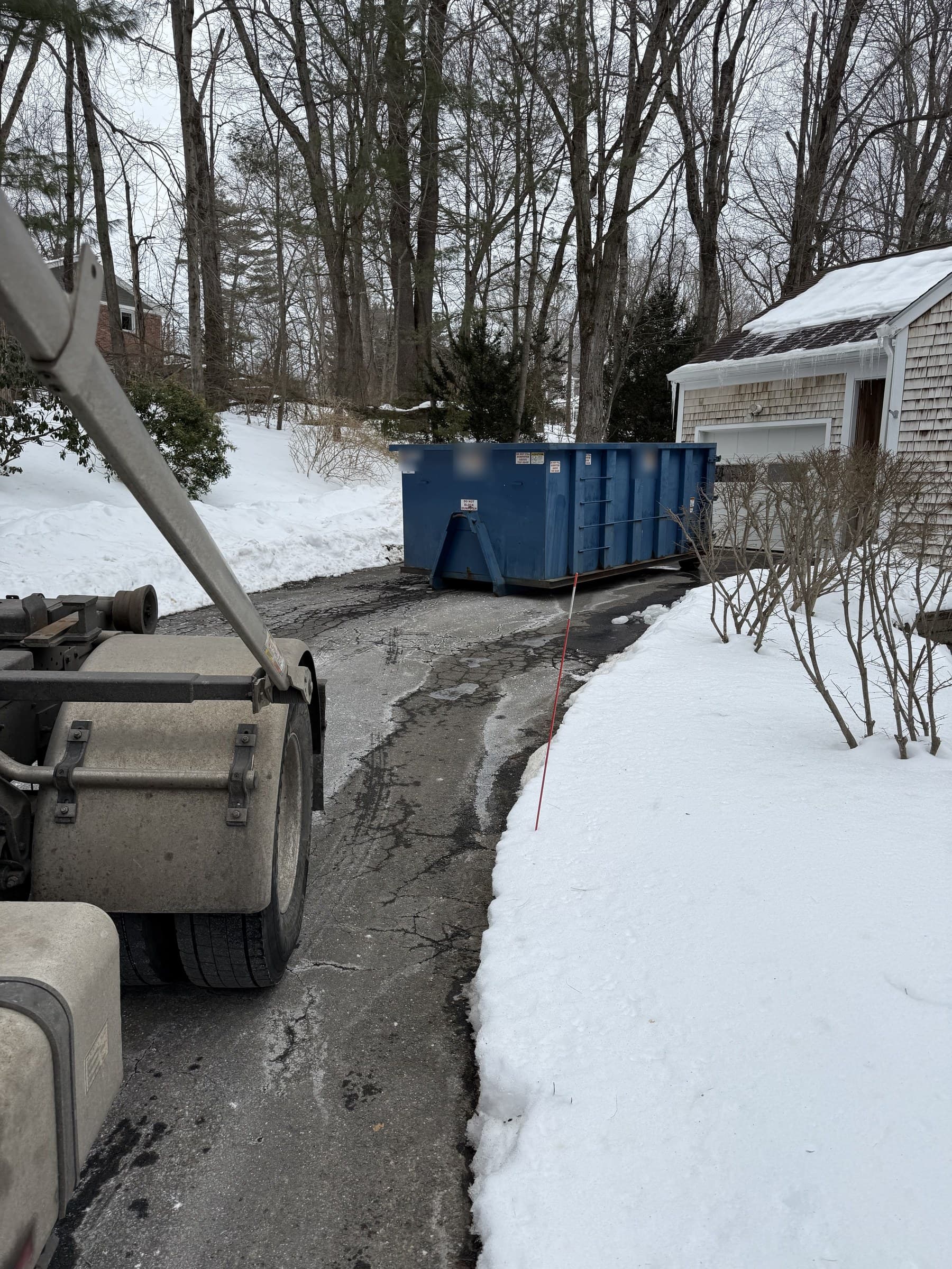 Roll-off truck beside a blue dumpster in a snowy driveway