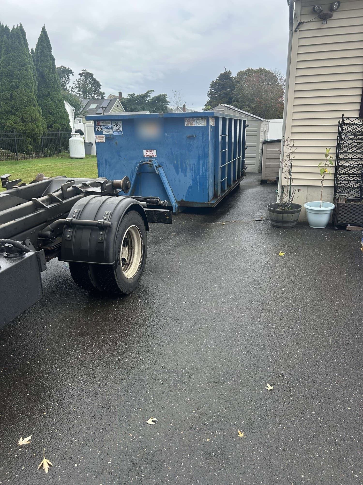 Hook-lift truck in front of a blue roll-off dumpster in a wet driveway