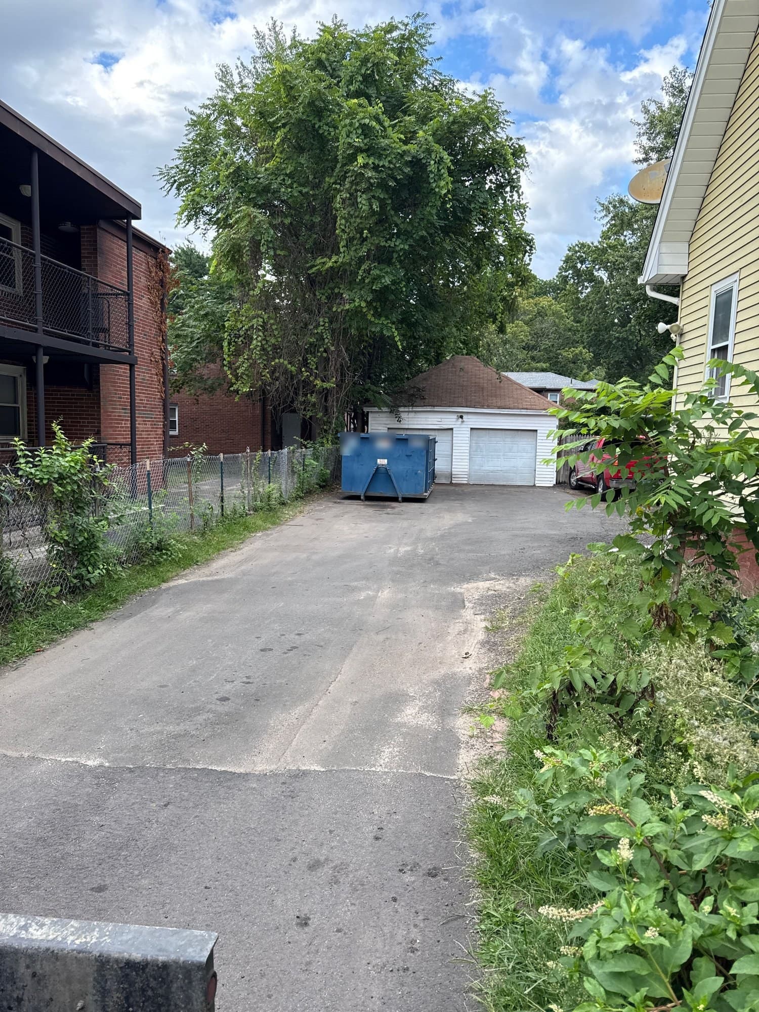 Blue roll-off dumpster in a long driveway by a detached garage