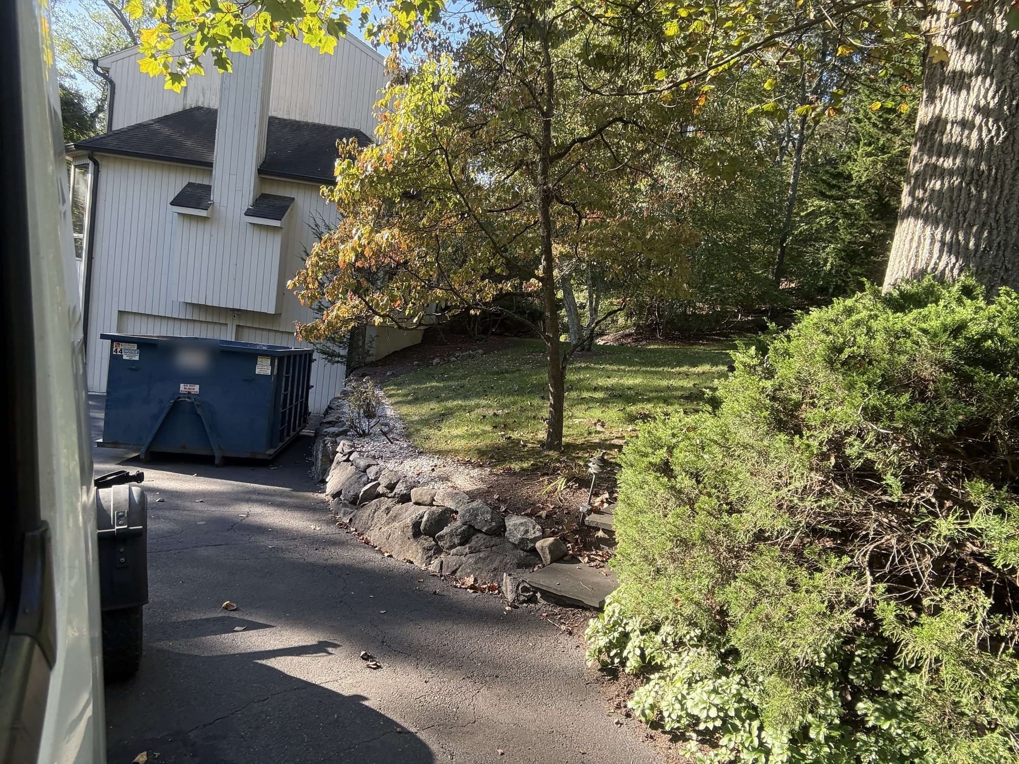 Blue roll-off dumpster at the top of a curved driveway