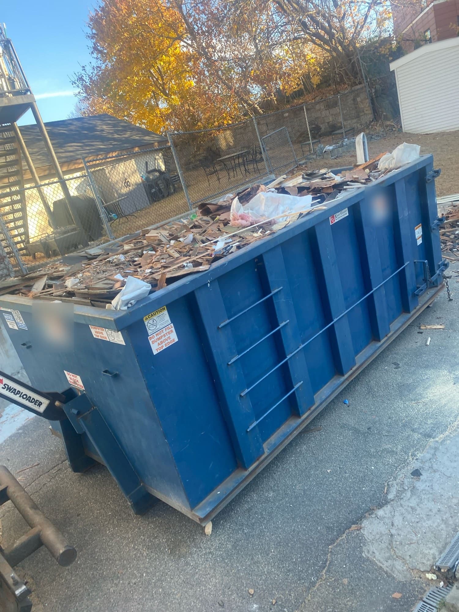Roll-off dumpster full of wood and shingle demolition debris in a driveway