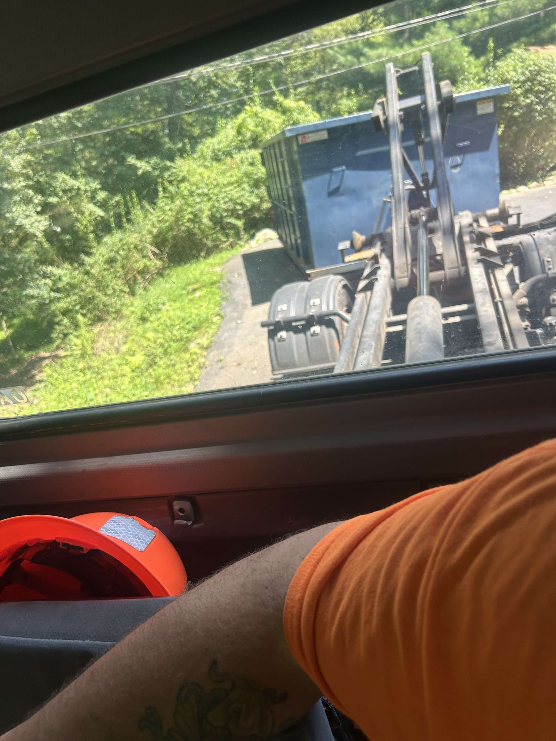 View from a truck cab as a hook-lift truck lines up with a blue roll-off dumpster on a driveway