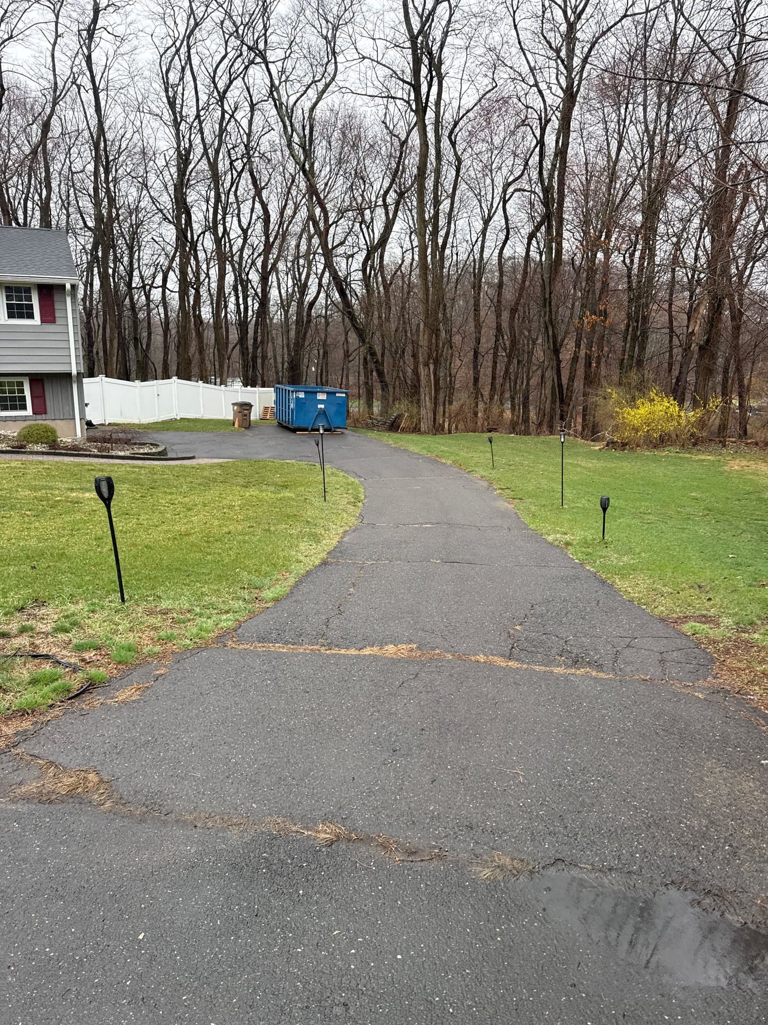 Blue roll-off dumpster at the end of a long residential driveway