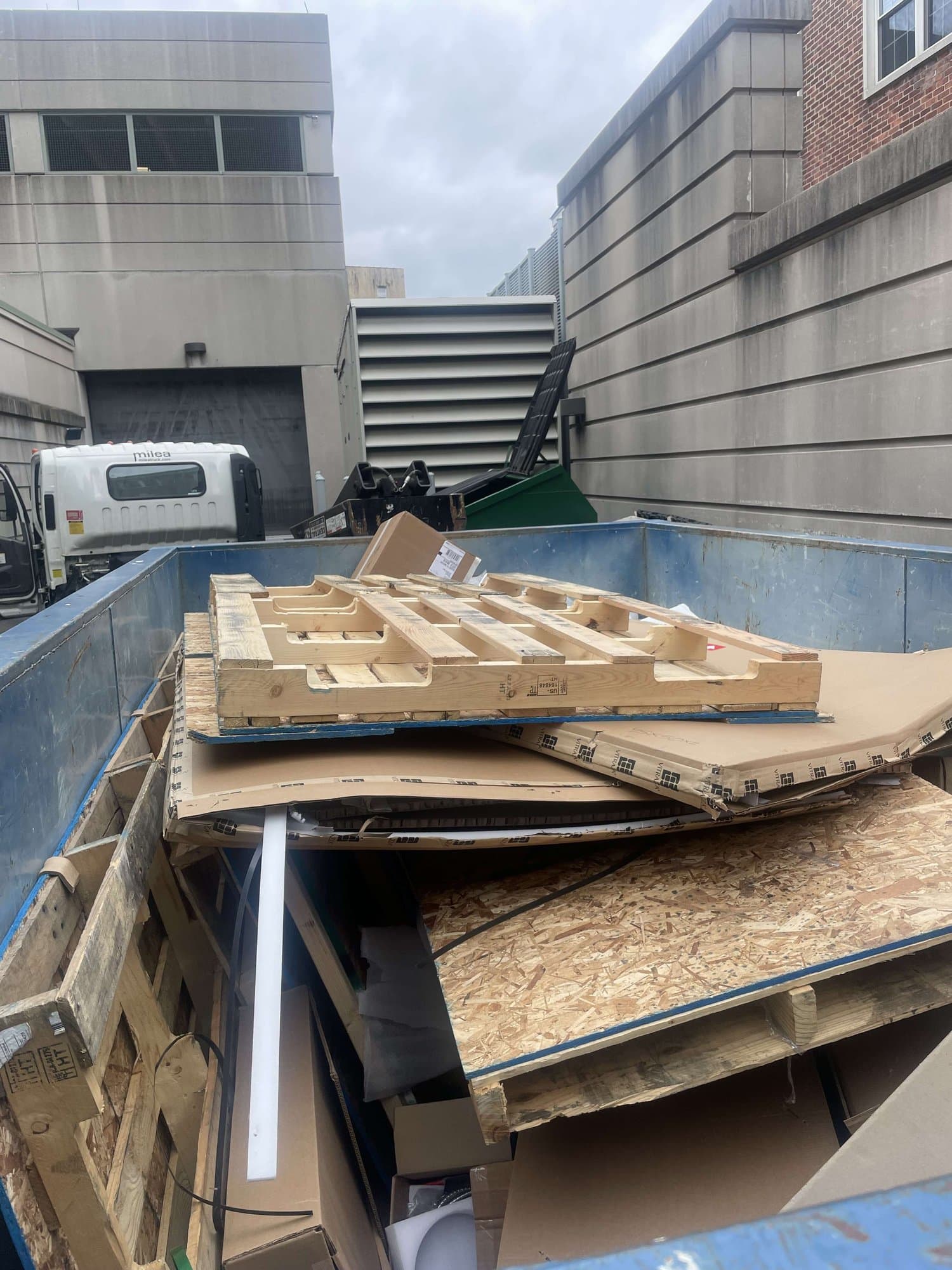 Blue roll-off dumpster loaded with pallets, OSB and cardboard in a loading alley
